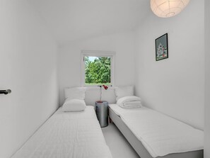 A small, white room with two single beds, a window with a view of greenery, a trash bin, and a framed picture on the wall. - "Franki" - 1.8km from the sea by Interhome (Faxe)