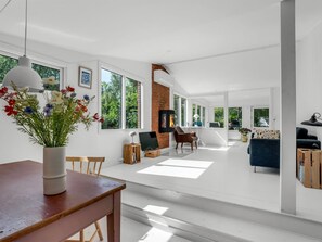Un vaste espace de vie doté d’une cheminée, de grandes fenêtres et d’une table à manger avec des chaises.