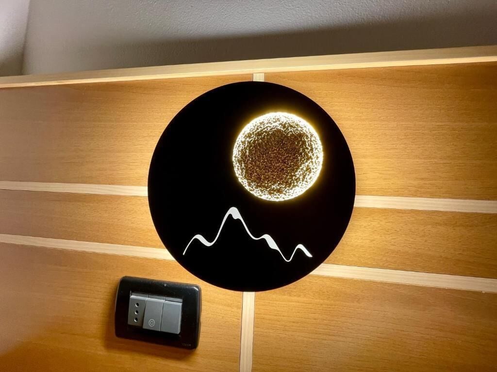 A wall-mounted light fixture with a circular design and a mountain silhouette.