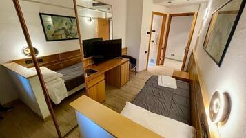 Una camera d'albergo con un letto, una scrivania con televisore, uno specchio e una porta.