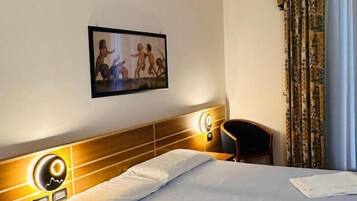 Habitación de hotel con cama, mesita de noche, silla, cuadro en la pared y ventana con cortinas.
