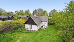 Een wit huis met een zwart dak, omringd door een verzorgd gazon en weelderige begroeiing.