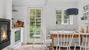Een keuken met een open haard, een eettafel met stoelen en een raam met uitzicht op groen.