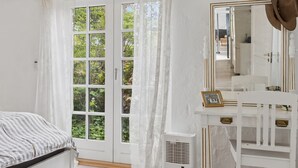 Een slaapkamer met een bed, een groot raam met gordijnen, een spiegel met een hoed, en een radiator.