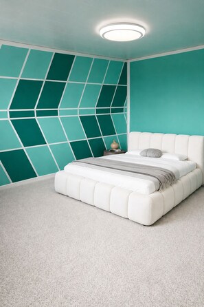 Ein Schlafzimmer mit einem weißen Bett, türkisfarbenen Akzentwänden, einem geometrischen Wandmuster und einer runden Deckenleuchte.