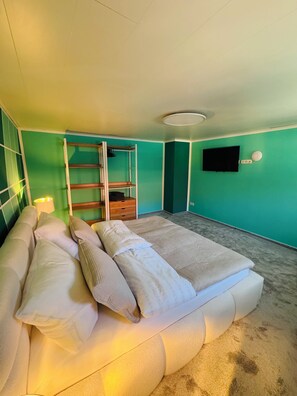 A bedroom with a bed, a TV, a shelf, and a lamp.