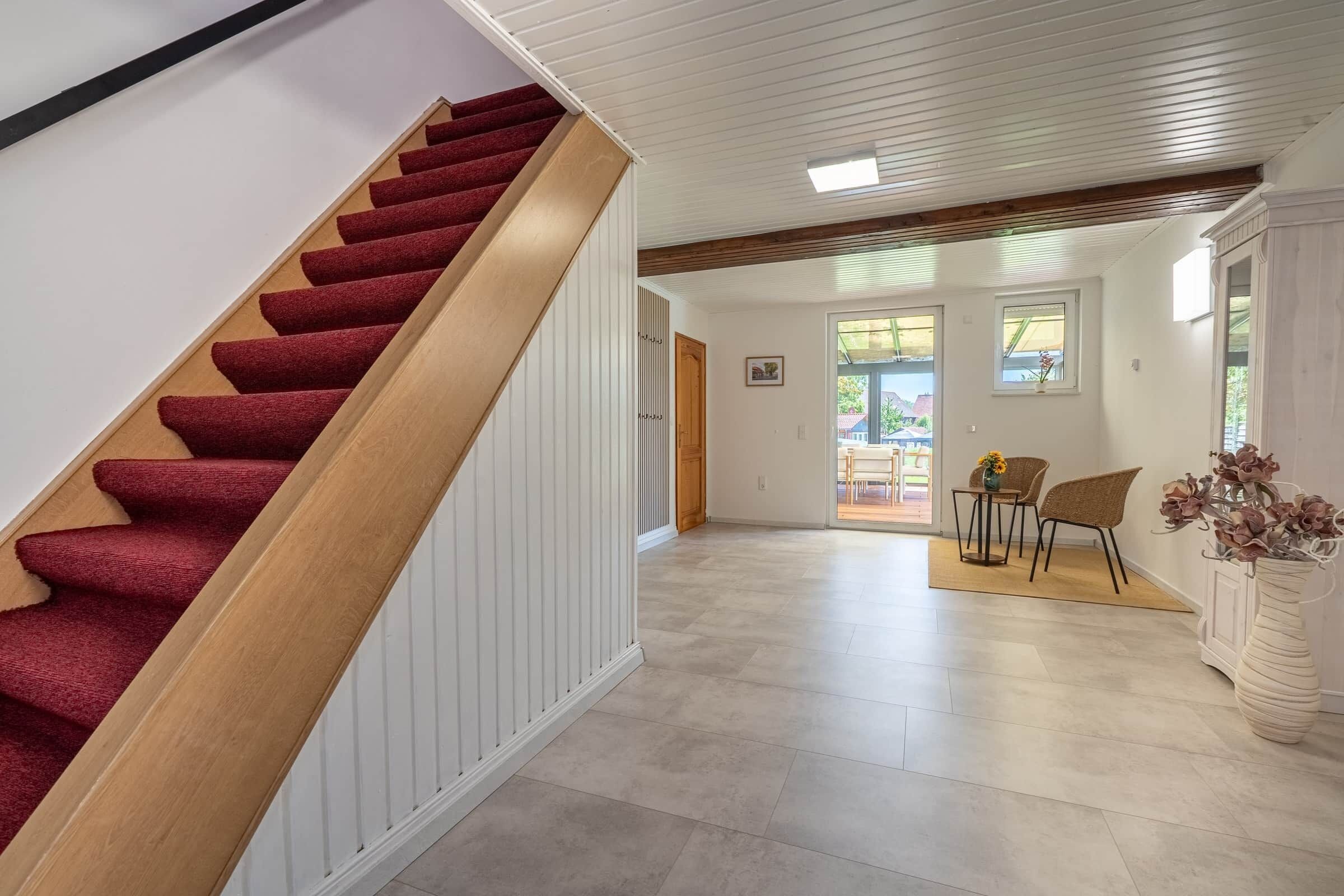 A staircase with a red carpet leading to a room with a wooden ceiling and a view of the outside.