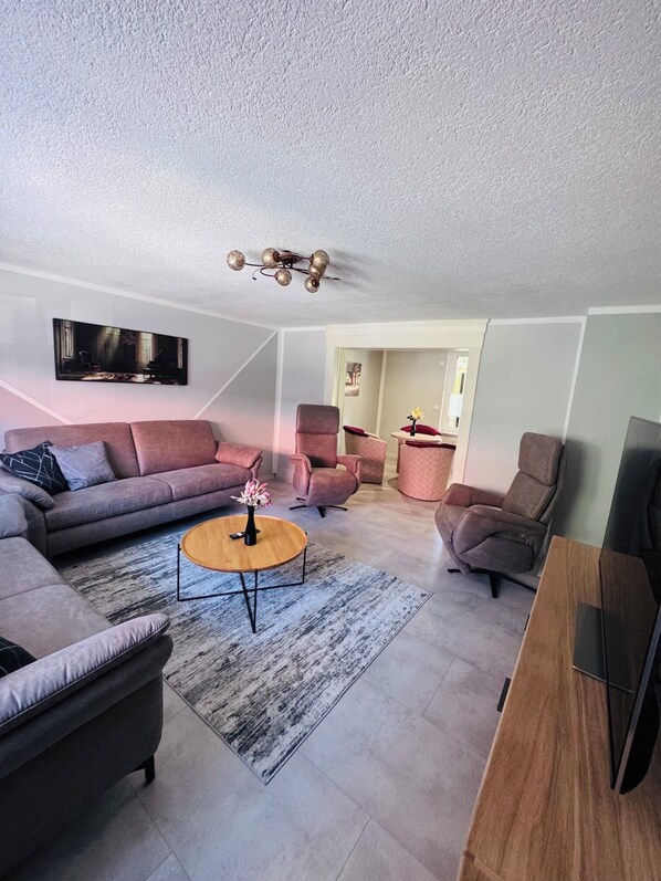 Un salon moderne avec un canapé, des fauteuils, une table basse et un téléviseur fixé au mur.