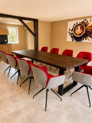 A modern dining area with a long wooden table and red and grey chairs.