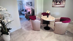 A modern living room with a round table and two chairs, a sofa, and a potted plant.