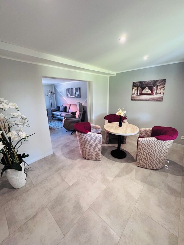 A modern living room with a round table and two chairs, a sofa, and a potted plant.