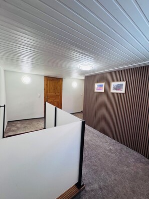 A corridor with a wooden door, a white partition, and a wall with vertical wooden slats.