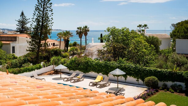 A rooftop pool area with lounge chairs and umbrellas, surrounded by greenery and overlooking a coastal view. - New Listing | Exclusive Ocean View Villa | 2Min to Beach (Armação de Pêra)