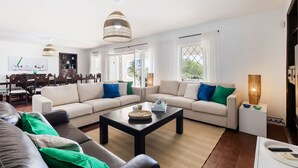 A modern living room with a sofa set, a coffee table, and a dining area with chairs and a table. - New Listing | Exclusive Ocean View Villa | 2Min to Beach (Armação de Pêra)