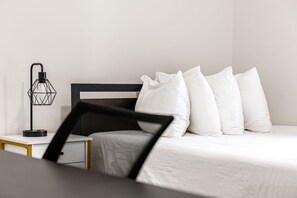 Ein Bett mit weißer Bettwäsche, einem schwarzen Kopfteil und einer Nachttischlampe mit geometrischem Design.
