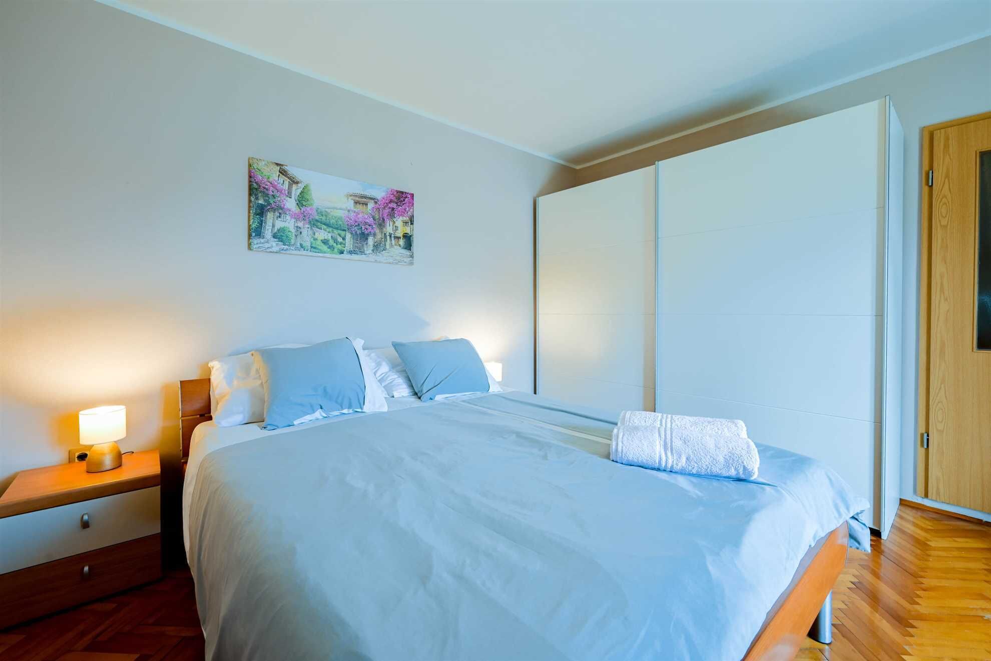 A bedroom with a bed, nightstand, and a painting on the wall.