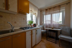 Une cuisine compacte équipée d’une cuisinière à gaz, d’un évier et de meubles de rangement en bois. On y trouve également un petit coin repas avec une table et une chaise.