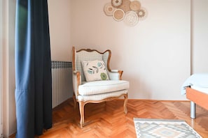 Une pièce dotée d’un parquet en bois disposé en motif de chevron, d’un fauteuil en bois avec un coussin, d’un tapis à motifs et d’un élément décoratif mural.
