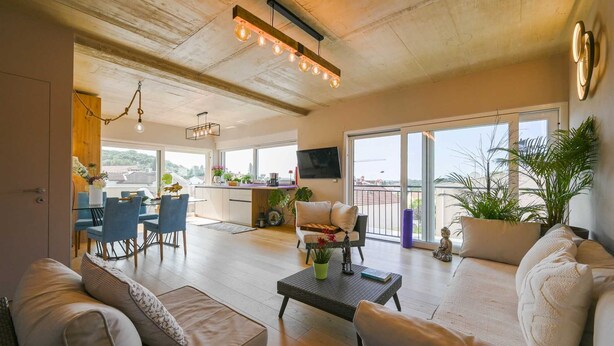 A spacious living area with a dining table, sofas, and a balcony with plants. - Stela Vela Apartment (Rovinj)