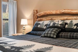A bed with a forest-themed headboard, a lamp, and a view of the outdoors.
