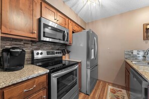 A kitchen with wooden cabinets, a stainless steel refrigerator, a microwave, a stove, and a coffee maker.