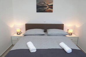 A neatly made bed with two pillows, two bedside lamps, and a painting above the bed. - Apartment Stella Maree 1 (Okrug)