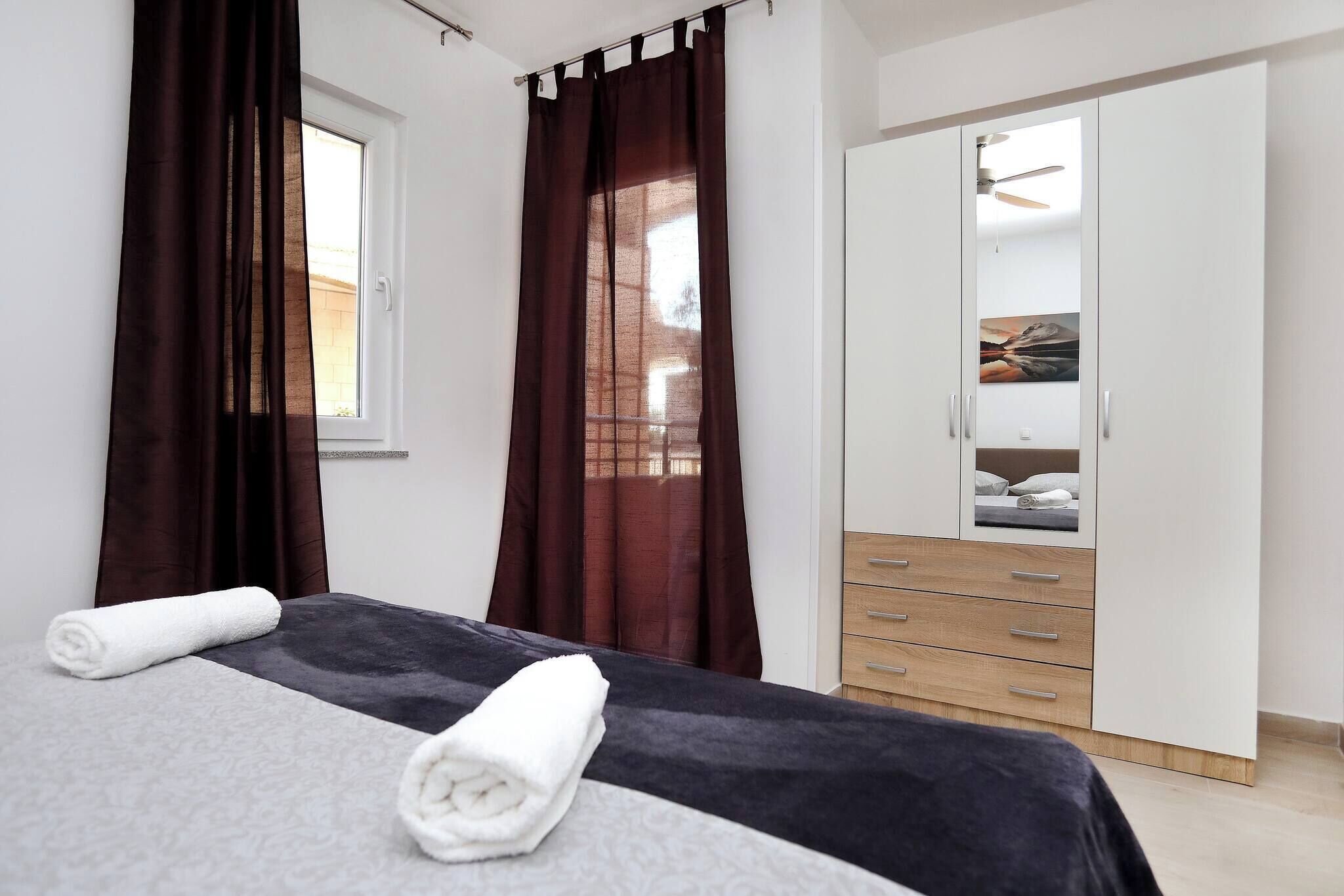 Een slaapkamer met een bed, een kledingkast, een raam met gordijnen en een plafondventilator.