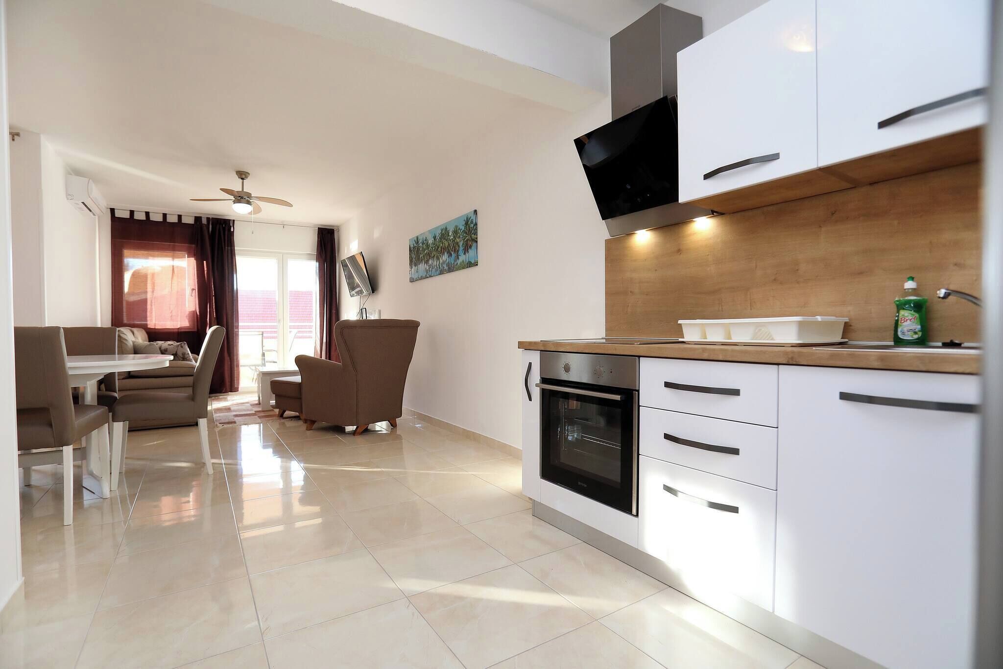 A modern kitchen with white cabinets, a built-in oven, and a flat-screen TV.
