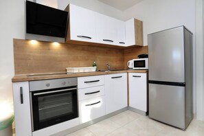 A modern kitchen with white cabinets, a stainless steel refrigerator, an oven, a microwave, and a wooden countertop. - Apartment Stella Maree 1 (Okrug)