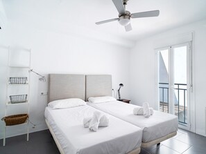 Ein modernes Hotelzimmer mit zwei Betten, einem Deckenventilator, einem Balkon mit Blick und einer weißen Farbgestaltung.