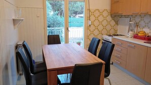 Un coin repas avec une table et des chaises en bois, une cuisine avec des meubles en bois et une porte-fenêtre coulissante donnant sur un balcon.