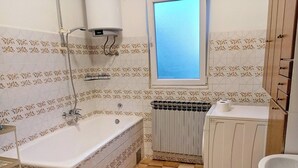 Une salle de bain avec une baignoire, une fenêtre, un radiateur et un lavabo.
