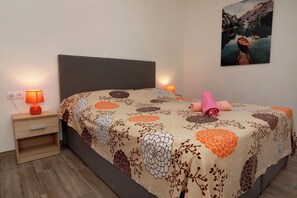 Ein ordentlich bezogenes Bett mit floralem Überwurf, zwei Nachttischlampen, ein Nachttisch und ein Bild an der Wand.