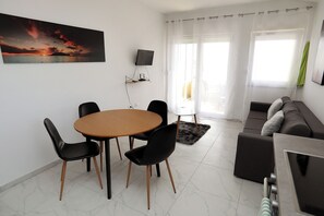 Ein Wohnzimmer mit einem runden Tisch, schwarzen Stühlen, einer Couch, einem Fernseher und einem Sonnenuntergangsbild.