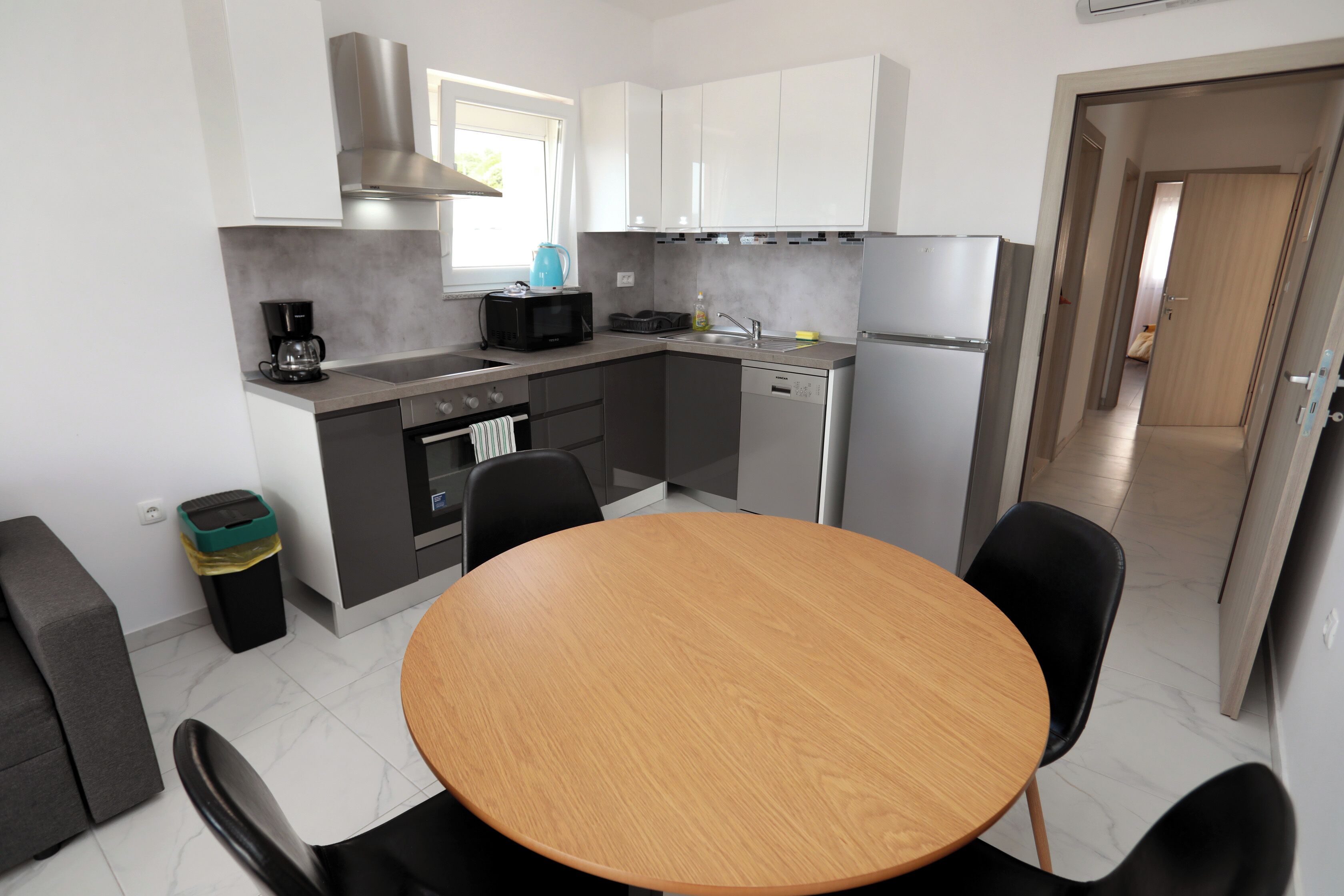 Una cocina compacta con una mesa redonda, sillas negras, microondas, cafetera y un cubo de basura.