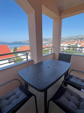 Ein Balkon mit Tisch und Stühlen, mit Blick auf eine Küstenstadt mit roten Dächern.