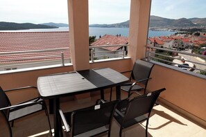 Ein Balkon mit Tisch und Stühlen, der Blick auf eine Küstenstadt mit roten Dächern und einem Gewässer freigibt.