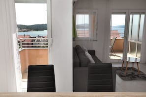 A balcony with a sofa and chairs, a table, and a view of the sea and hills. - Nice 2 Bed Apartment (Okrug)