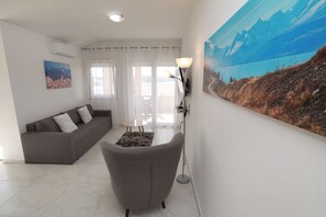 A living room with a grey sofa, a small round table, a floor lamp, and a large landscape painting on the wall. - Nice 2 Bed Apartment (Okrug)