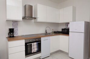 A modern kitchen with white cabinets, a stainless steel range hood, a dishwasher, and a refrigerator. - Nice 2 Bed Apartment (Okrug)