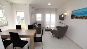 A modern living room with a dining area, a sofa, a TV, and a painting on the wall. - Nice 2 Bed Apartment (Okrug)