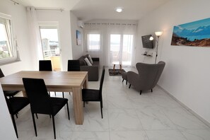 A modern living room with a dining area, a sofa, a TV, and a painting on the wall. - Nice 2 Bed Apartment (Okrug)