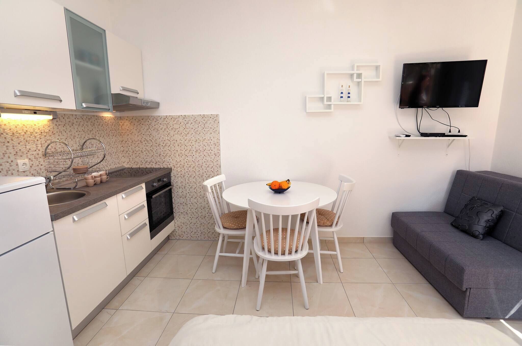 A compact kitchen with a dining area, a sofa, and a TV mounted on the wall.