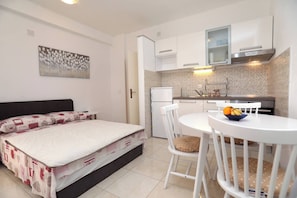 A compact room with a bed, a small kitchenette, a dining table with chairs, and a wall-mounted painting. - Apartment Stella Maree 3 (Okrug)