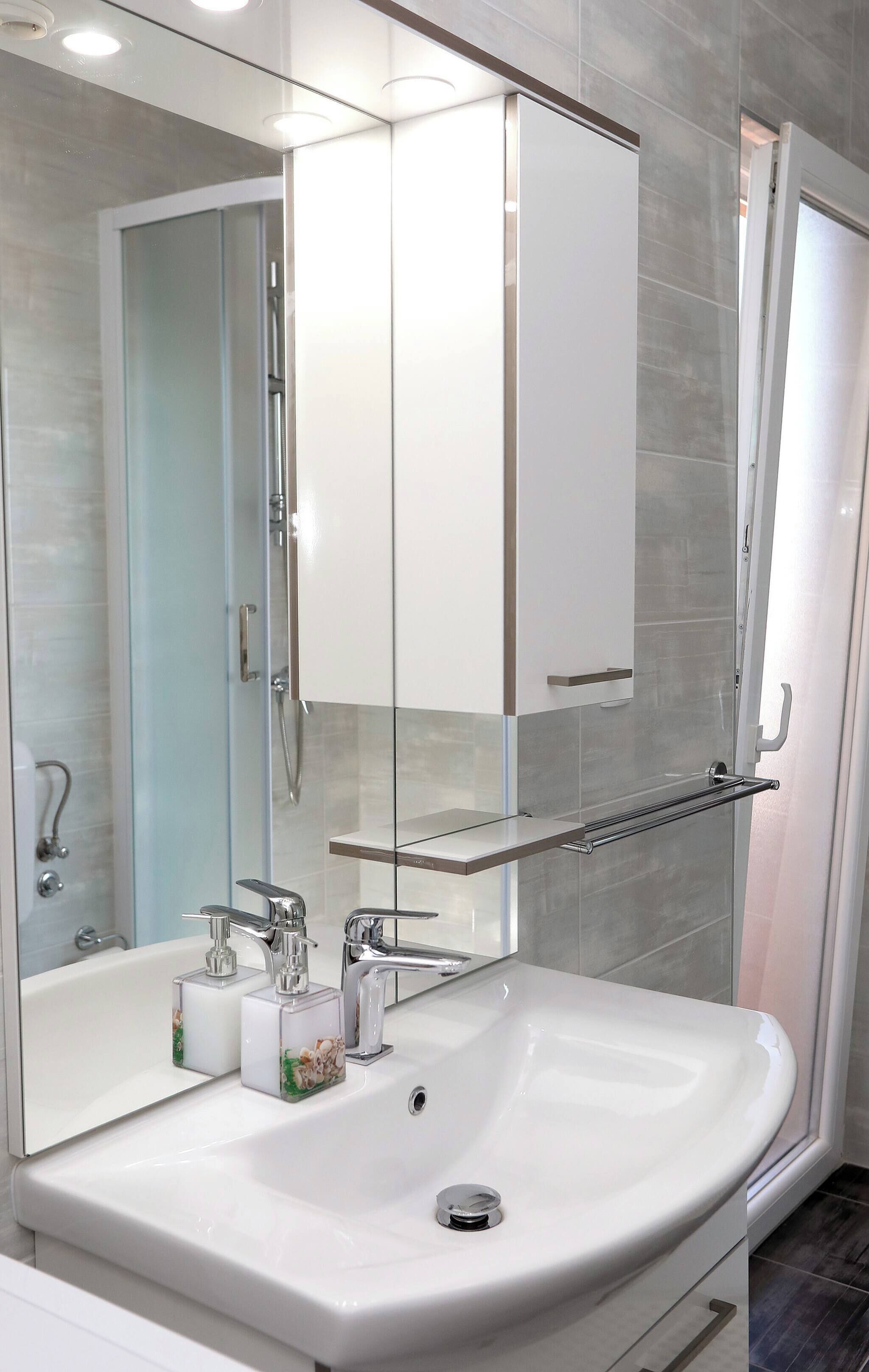 A modern bathroom with a white sink, a glass shower enclosure, and a mirrored cabinet above the sink.
