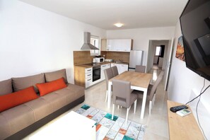 A modern living room with a sofa, a dining area with chairs, a kitchen with cabinets, and a TV mounted on the wall. - Charming 2-bedroom Apartment With Stunning Views in Okrug Gornji (Okrug)