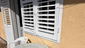 A small outdoor seating area with a round table and two chairs, a window with shutters, and a textured wall. - Sunny Apartment in Trogir (Trogir)