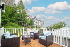 A deck with wicker furniture and a table, overlooking a residential area with houses and greenery.