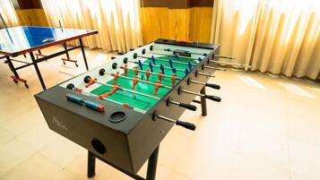 Una mesa de fútbol de diseño azul y naranja, una mesa de ping pong y una ventana con cortinas.
