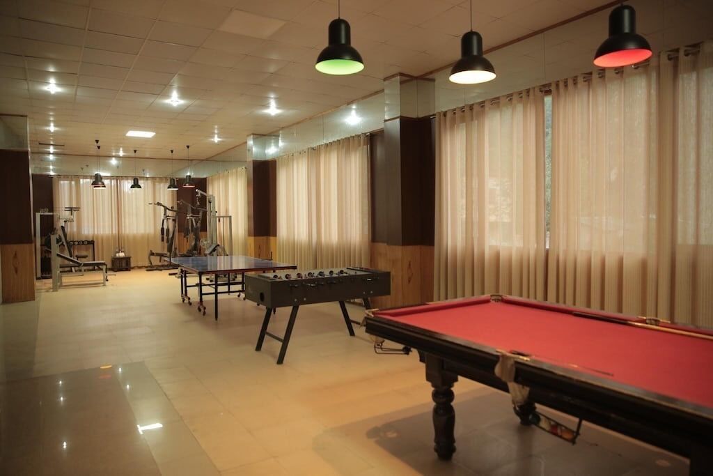 Mesa de billar, mesa de futbolín y mesa de ping pong en una habitación con ventanas amplias y cortinas.